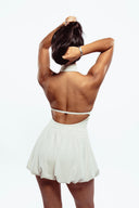 Person wearing a white dress with a halter top and pleated skirt on a white background